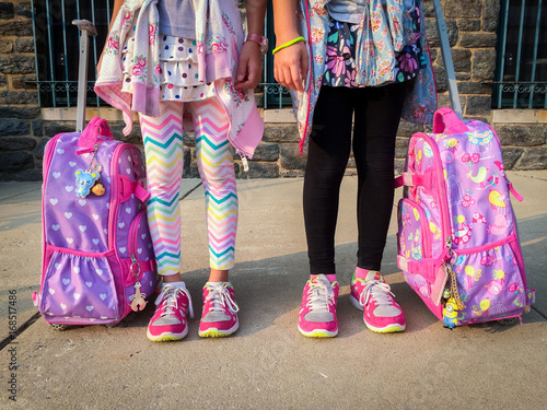 Girls first day of elementary school with rolling backpacks for saving their backs with heavy boods