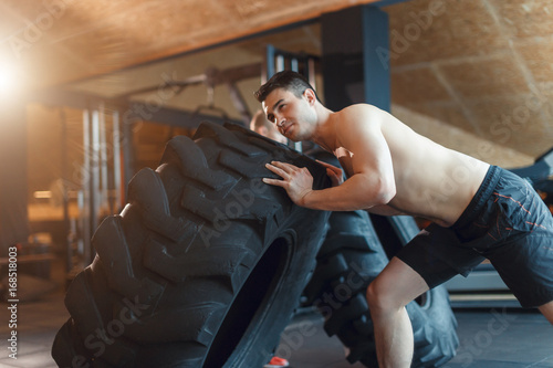 two Fit male athlete working out with a huge tire, turning and flipping in the gym. Cross fit man exercising with big tire. photo