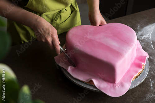 Fotografía Unrecognisable woman in bakery decorating heart shaped wedding cake with pink fo
