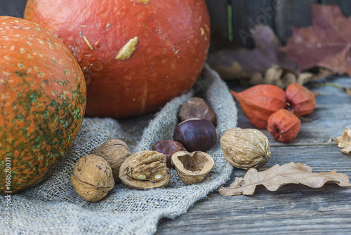 autumn composition with orange pumpkins, nuts and dry leaves on rustic background photo