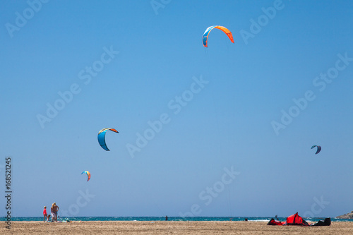 People practicing Kitesurfing. Beach on the peninsula Prasonisi, Rhodes. Colorful kites on the sea shore. Blue sea and windsurfing.