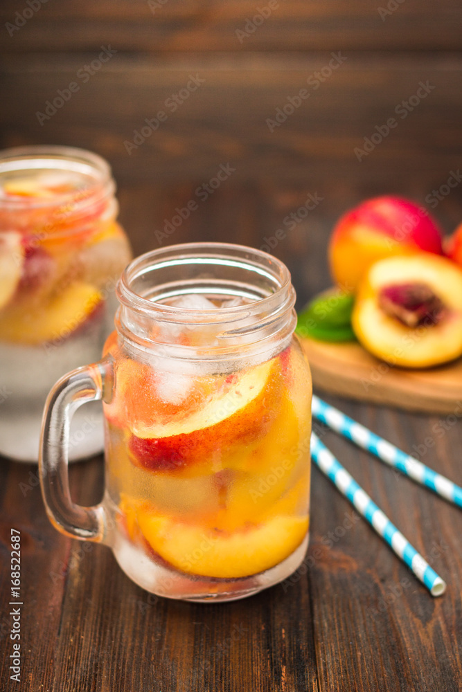 Mason jar glass of homemade peach iced water on a rustic wooden background. Mason jar glass of homemade peach iced water on a rustic wooden background.