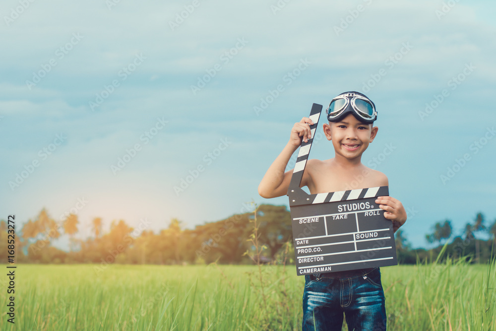 Kid playing film clapper board against summer sky background. Film director concept. Kid playing film clapper board against summer sky background. Film director concept.
