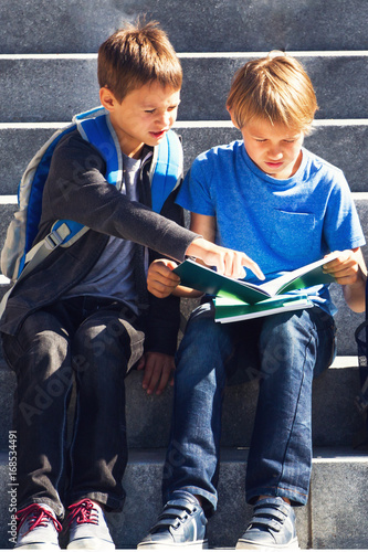 Two boys reading, doing homework outdoors. Back to school concept.