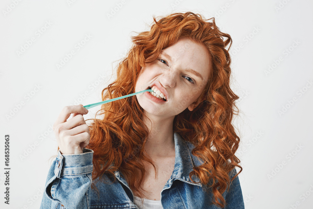 Young cool brutal redhead girl in jean jacket chewing gum looking at camera over white background. Young cool brutal redhead girl in jean jacket chewing gum looking at camera over white background.