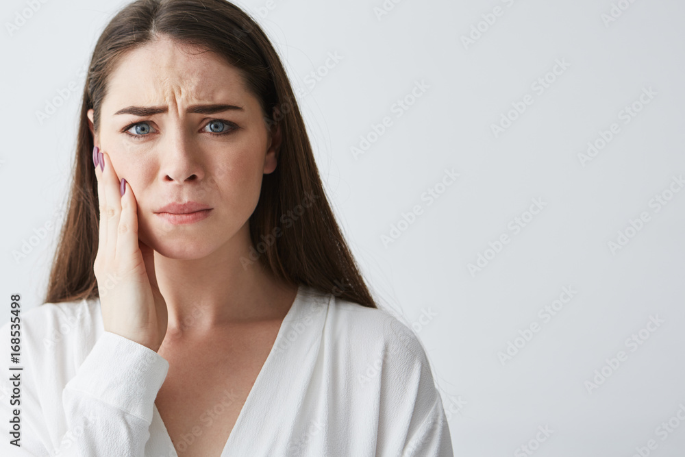 Sad upset young girl looking at camera with hand on face over white background. Sad upset young girl looking at camera with hand on face over white background.