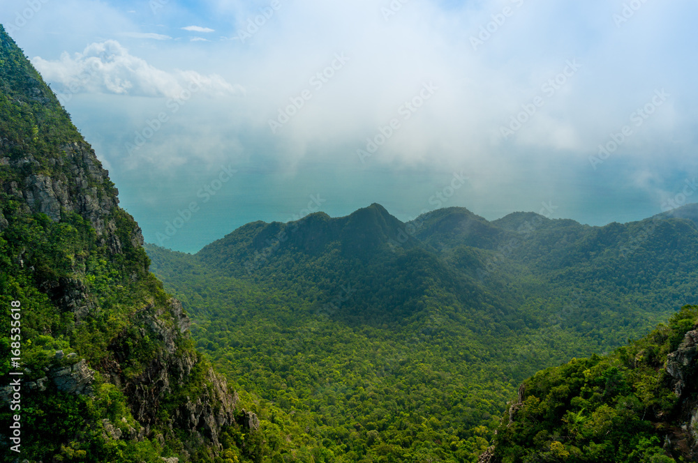 Obraz premium Beautiful tree covered mountains fading into the distance with cloudy skies and fog rolling between them. Shot in Langkawi near the Machincang mountain