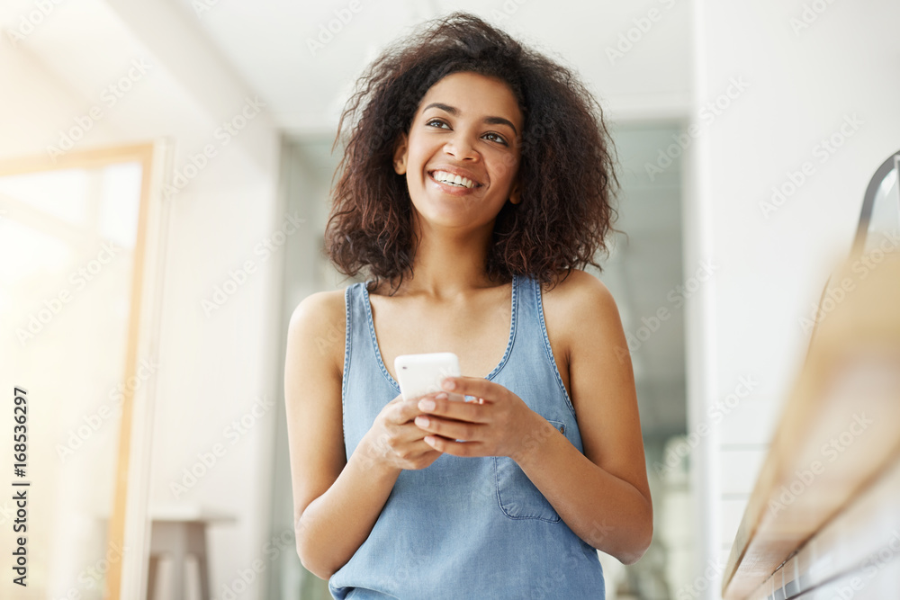 Dreamy beautiful african girl smiling thinking dreaming holding phone sitting in cafe. Dreamy beautiful african girl smiling thinking dreaming holding phone sitting in cafe.