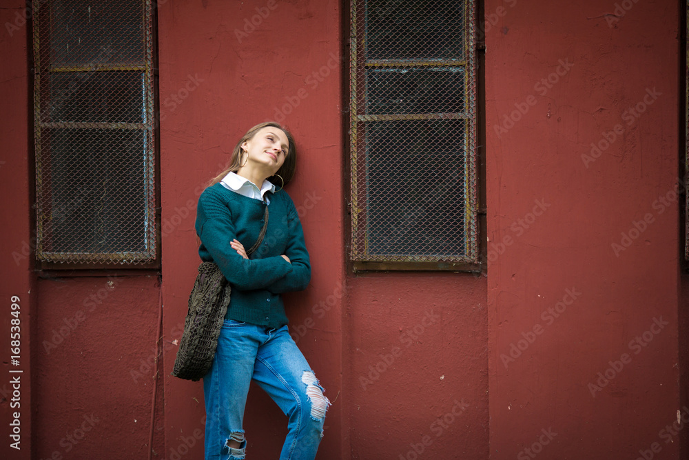 Enjoying resting woman standing near red metallic wall, urban background