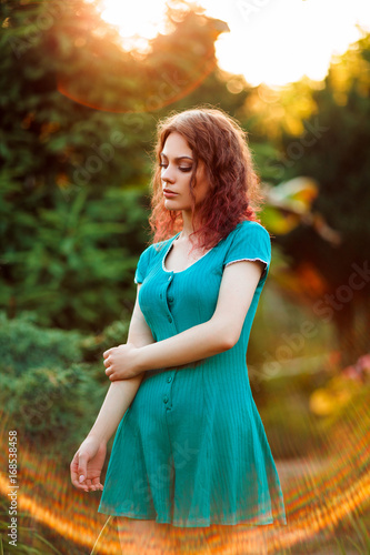Fototapeta Naklejka Na Ścianę i Meble -  Beautiful girl with curly hair in vintage dress on sunset. Background of foliage with sunbeams. Perfectly retouched.