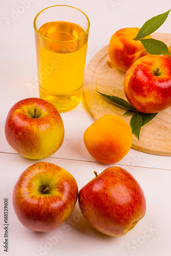 Glass of juice and ripe apples and peaches on a wooden table