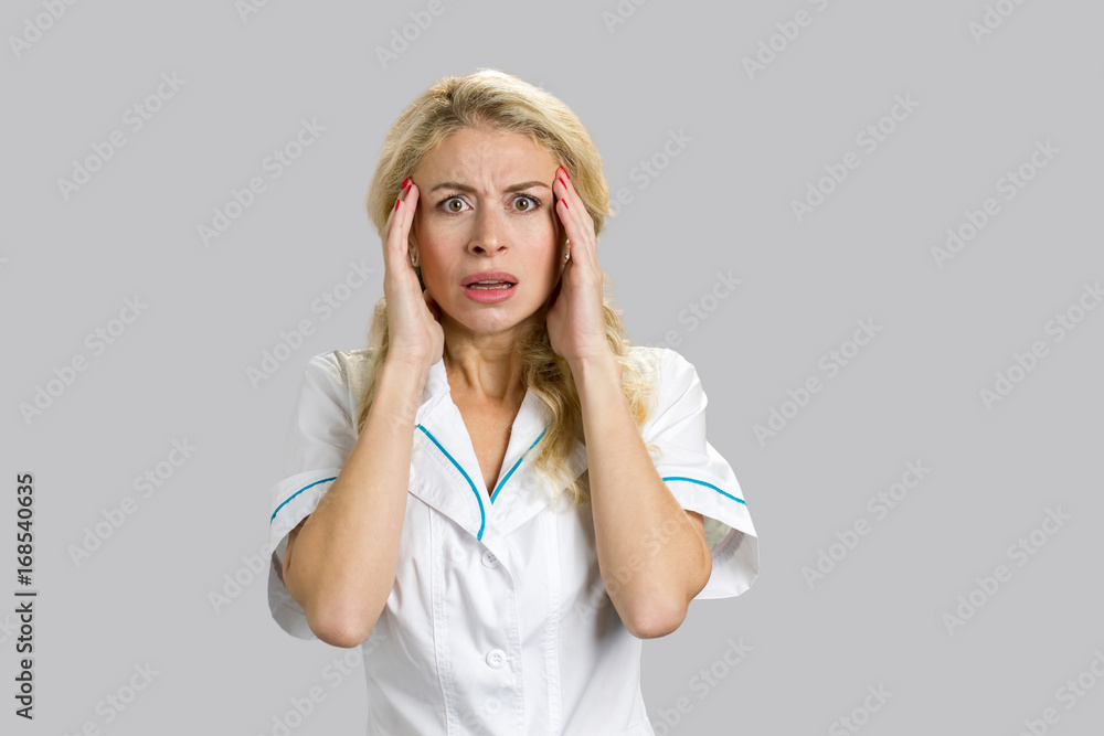 Shocked and scared female nurse or doctor. Attractive young nurse looking surprised and frustrated over grey background. Shocked and scared female nurse or doctor. Attractive young nurse looking surprised and frustrated over grey background.