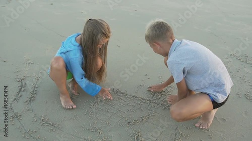 Little sister and brother draw on sand.