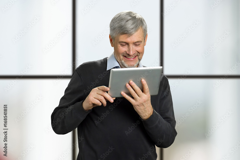 Mature man smile reading news on tablet. Happy senior man looking on pc tablet and smiling on window background. Mature man smile reading news on tablet. Happy senior man looking on pc tablet and smiling on window background.