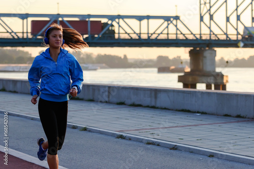 Young woman jogger running by the river in the morning