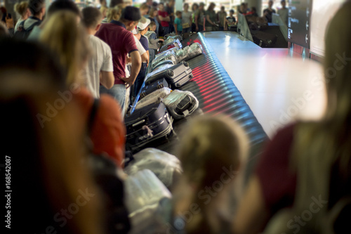 Suitcase on luggage conveyor belt at baggage claim at airport. Lines of people waiting for their baggagemorning