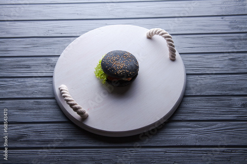 Black wooden serving tray with black burger, potato wedges and ketchup, vertical shot on a grey stone background photo