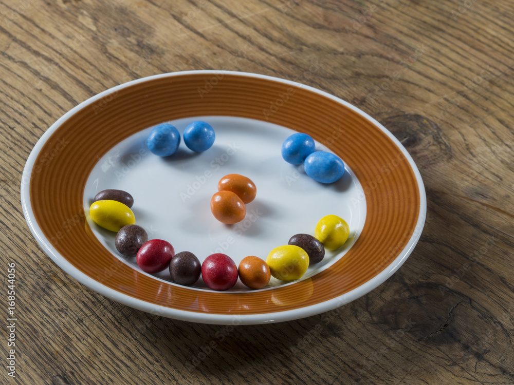 smile from colorfull candy bonbon white brown plate on wooden desk smile from colorfull candy bonbon white brown plate on wooden desk