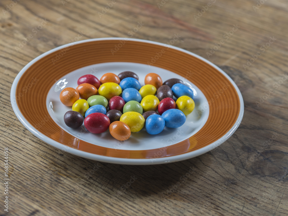colorful bonbon candy on white brown plate on wooden desk colorful bonbon candy on white brown plate on wooden desk