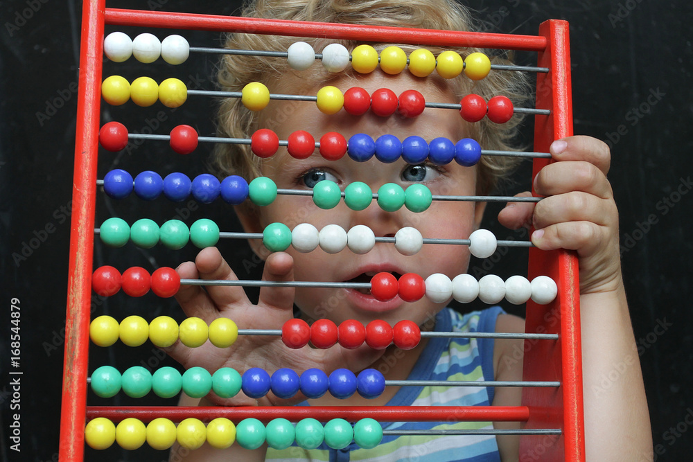 A small toddler boy looks through through the bright bones of wooden accounts. An ancient machine for performing arithmetic operations and a new generation. A small toddler boy looks through through the bright bones of wooden accounts. An ancient machine for performing arithmetic operations and a new generation.