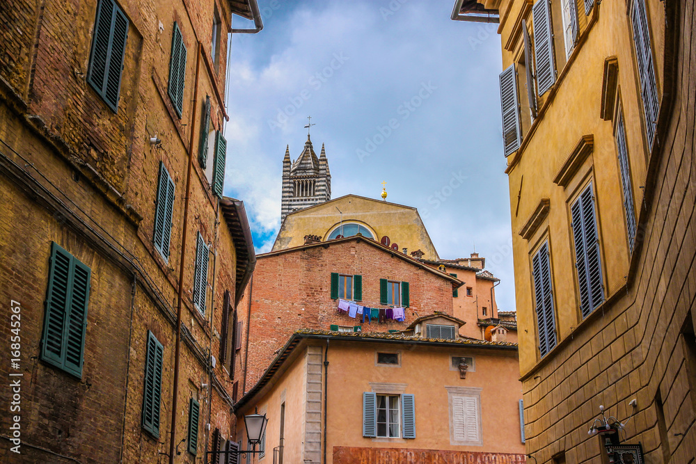 Street of medieval Siena with view on historical center and Duomo cathedral. Tuscany, Italy.