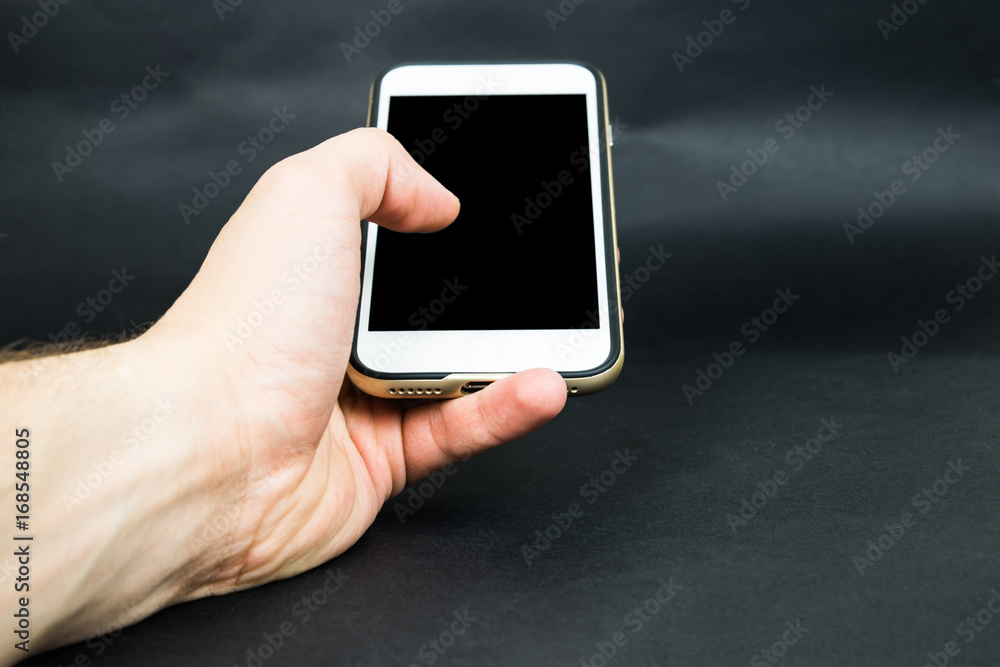 Hand holds mobile phone with blank screen on dark background Hand holds mobile phone with blank screen on dark background