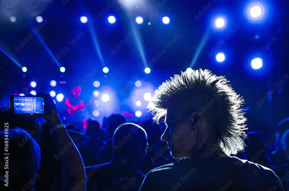 silhouettes of concert crowd and mohawk punk hair style in front of bright stage lights