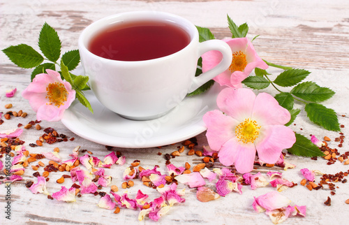Cup of hot tea with wild rose flower on old rustic wooden board