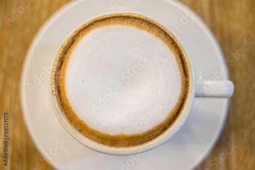A cup of cappuccino coffee on wooden table in the background of cafeteria