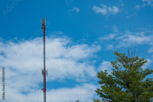 Mobile phone communication antenna tower with cloud on center blue sky background and tree
