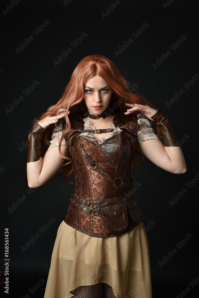 portrait of a red haired girl wearing steampunk costume. black studio background.