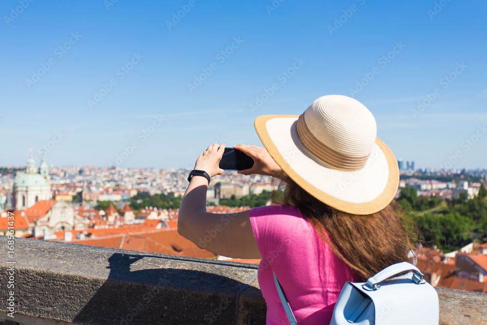 Woman taking pictures with smartphone. Stylish summer traveler woman in hat with camera outdoors in european city, Czech Republic, Europe