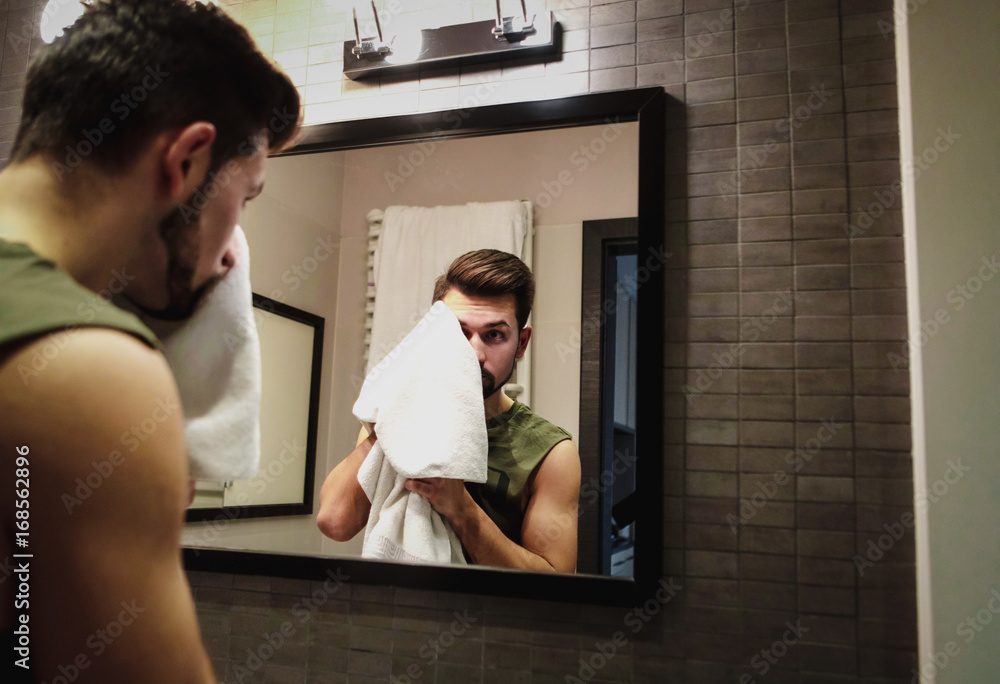 Fototapeta premium Reflection of young man in bathroom mirror looking on his face