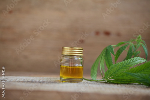 A cannabis leaf and a bottle of hemp oil on a wooden table