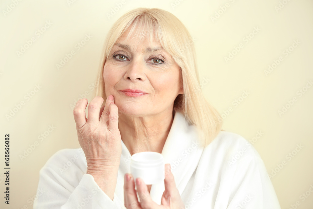 Senior woman applying cream onto face against light background Senior woman applying cream onto face against light background