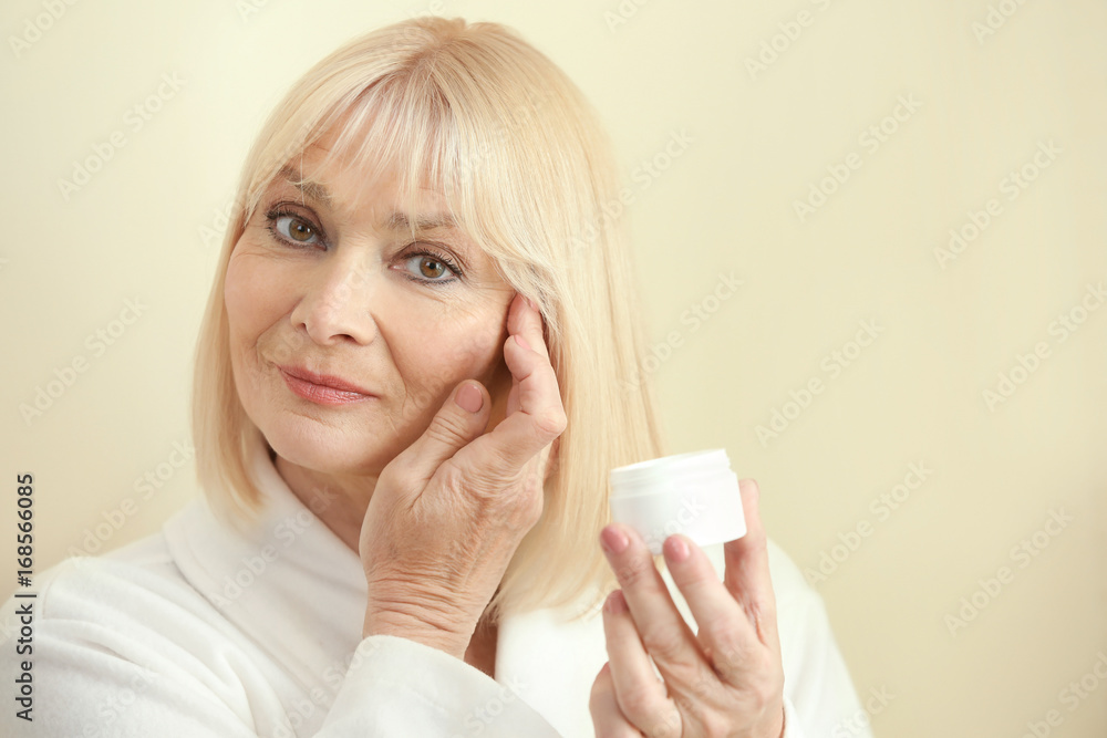 Senior woman applying cream onto face against light background Senior woman applying cream onto face against light background