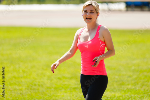 Portrait of a strong fit girl in sportswear running in the stadium. Beautiful girl runs in the stadium and listens to the player