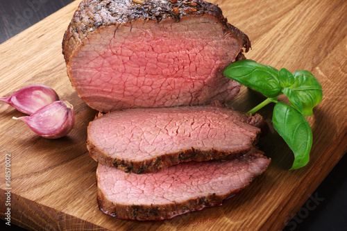 Baked meat, garlic and basil on a wooden background. Roast beef.