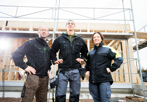 Carpenters Standing With Hands On Hips Against Incomplete Buildi