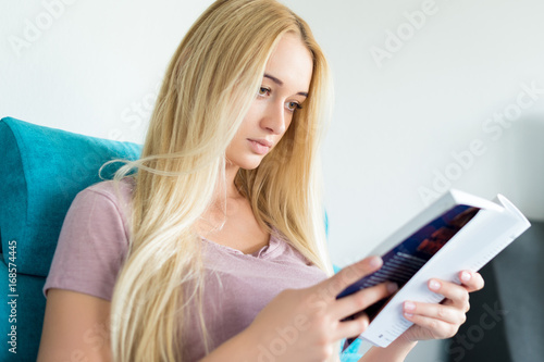 Beautiful young woman relaxing on the sofa at home, reading a book