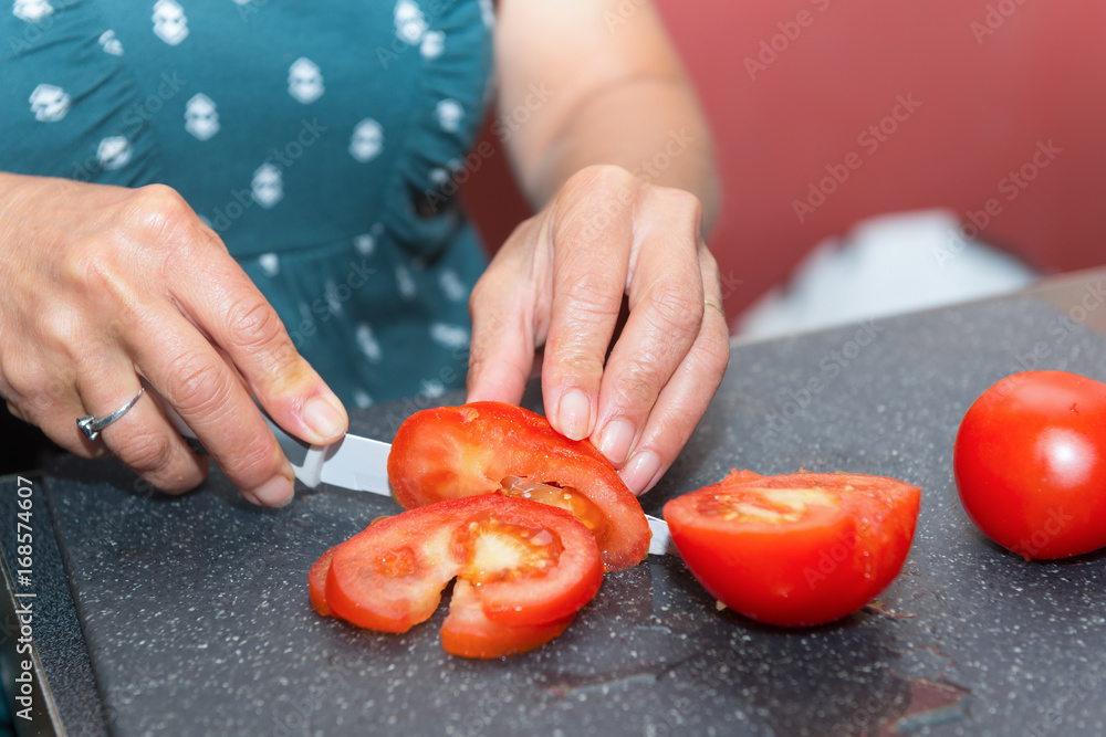 woman cutting tomato with the knife, on a plate woman cutting tomato with the knife, on a plate