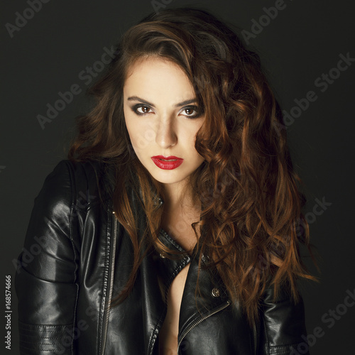 Beautiful young woman posing in black leather jacket over grey background. Fashion concept.