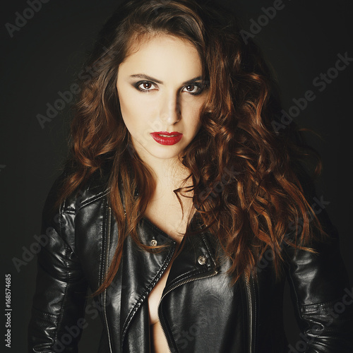 Beautiful young woman posing in black leather jacket over grey background. Fashion concept.