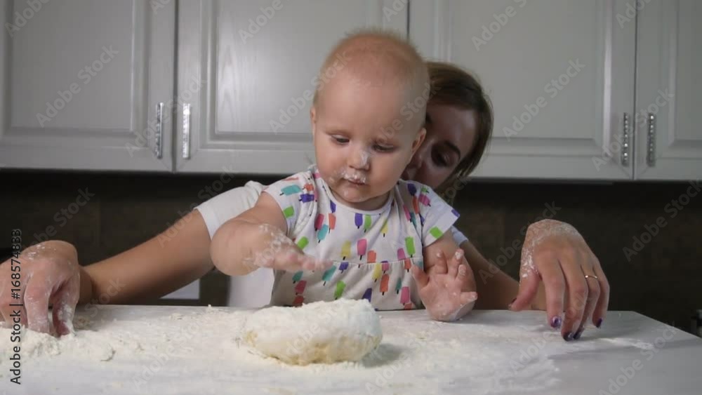 Young mother and her little daughter preparing dough on the table. Little baby playing with flour. Baker prepares the dough. Family girls having fun. Slowmotion shot