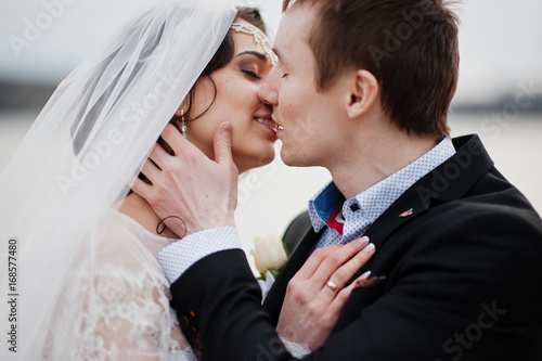 Close-up photo of a kissing wedding couple on the lakeside.