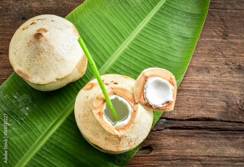 Two fresh coconut fruits ready to serve as beverage. Young coconut fruit cut open to drink sweet juice and eat. Flat lay on green banana leaf and wood background. 