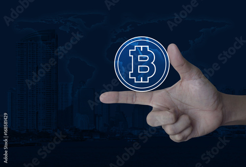 Bitcoin icon on finger over world map and modern city tower, Internet currency concept, Elements of this image furnished by NASA