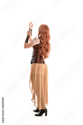 full length portrait of a red haired lady wearing steampunk inspired outfit, standing pose against a white background.