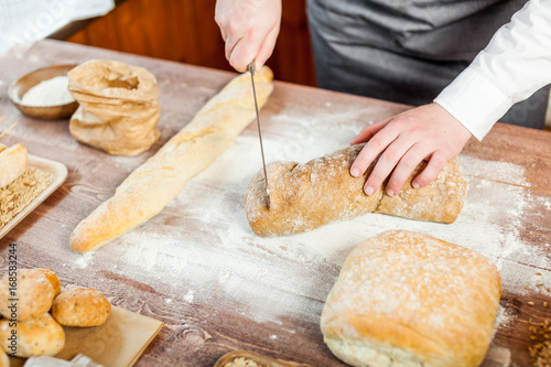 Male hands cutting fresh bread on the wooden table, selective focus