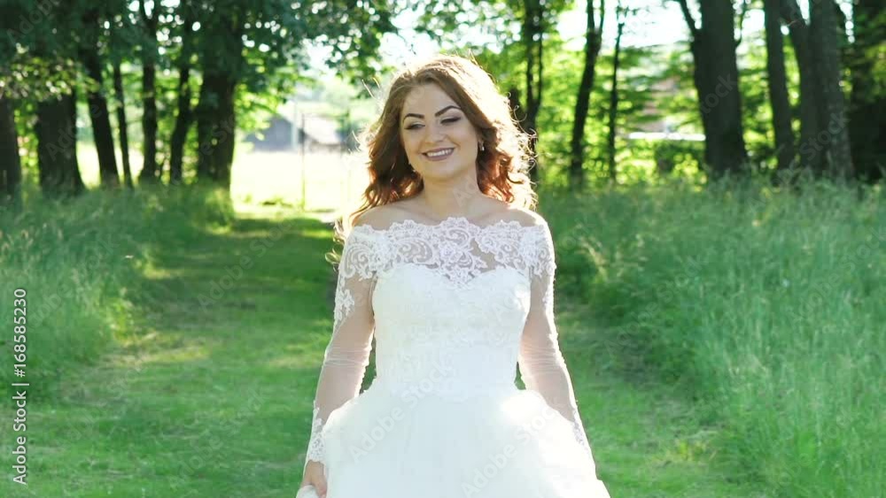 Pretty bride walks at camera in the sunny park. Slowly Pretty bride walks at camera in the sunny park. Slowly